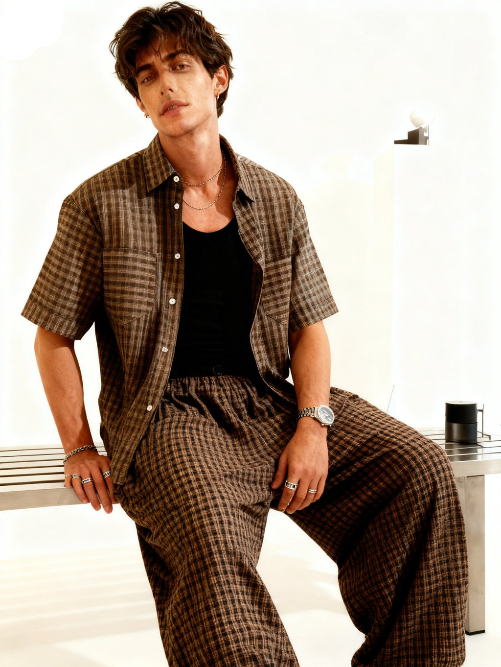 Man wearing a checkered shirt and pants sitting on a white surface.